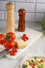 Ingredients for cooking: big tomatoes, small cherry tomatoes, parmesan cheese, oregano herb, salt and pepper mills on marble board