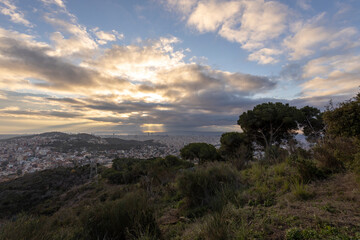 Picturesque landscape of Barcelona from the hill in the early morning. Sunbeams through the clouds. Dramatic sky over the city. Autumn in Barcelona, Spain.