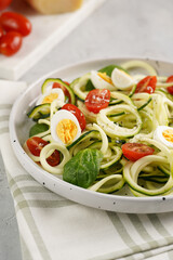 Keto paleo low-carb zoodles: zucchini noodles with parmesan cheese, cherry tomatoes, quail eggs on a checkered kitchen towel light grey surface