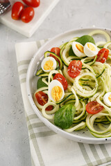Keto paleo low-carb zoodles: zucchini noodles with parmesan cheese, cherry tomatoes, quail eggs on a checkered kitchen towel light grey surface