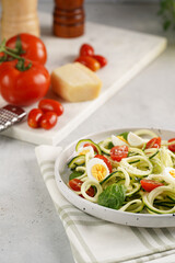 Keto paleo low-carb zoodles: zucchini noodles with parmesan cheese, cherry tomatoes, quail eggs on a checkered kitchen towel light grey surface