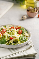 Keto paleo low-carb zoodles: zucchini noodles with parmesan cheese, cherry tomatoes, quail eggs on a checkered kitchen towel light grey surface