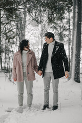 A millennial couple in love is standing under a tree from which snow is falling