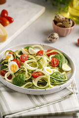 Keto paleo low-carb zoodles: zucchini noodles with parmesan cheese, cherry tomatoes, quail eggs on a checkered kitchen towel light grey surface