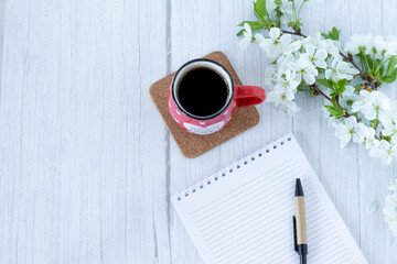 Cup of coffee and a blank notebook on a table with spring flowers in vintage style. Copy space. Top...