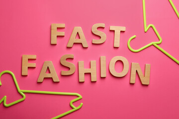 Phrase FAST FASHION made of wooden letters and bright hangers on pink background, flat lay