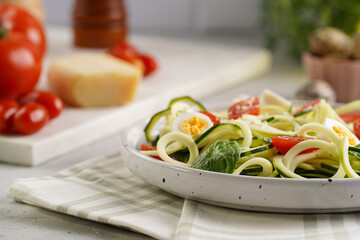 Keto paleo low-carb zoodles: zucchini noodles with parmesan cheese, cherry tomatoes, quail eggs on a checkered kitchen towel light grey surface