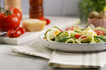 Keto paleo low-carb zoodles: zucchini noodles with parmesan cheese, cherry tomatoes, quail eggs on a checkered kitchen towel light grey surface