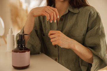 Obraz premium Close-up of young caucasian woman's hands with clean skin applying cream at home. Girl in green shirt sits at table. Spa and beauty concept