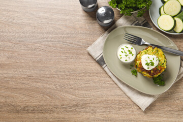 Delicious zucchini fritters with sour cream served on wooden table, flat lay. Space for text