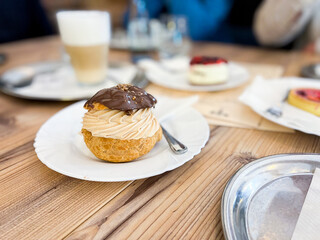 Chocolate choux pastry desset filled with buttercream served on white plate with restaurant table background