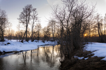 Winter landscape, trees near the river against the backdrop of sunset.