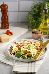 Keto paleo low-carb zoodles: zucchini noodles with parmesan cheese, cherry tomatoes, quail eggs on a checkered kitchen towel light grey surface