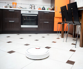 Robotic vacuum cleaner on ceramic tile floor in kitchen.
