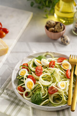 Keto paleo low-carb zoodles: zucchini noodles with parmesan cheese, cherry tomatoes, quail eggs on a checkered kitchen towel light grey surface