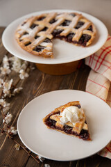 American cherry pie. A piece of  pie with a scoop of ice cream on a white plate in the foreground with a sprig of cherry blossoms. 
