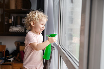 Housework. Cute curly child blonde girl with an emotion of joy helps to wash the windows in the...