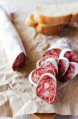 Traditional Catalan thin sausage - fuet. Pieces Pork sausage with mold with a few pieces of bread on craft paper. Vertical orientation.