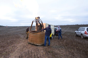 Preparations for ballooning: men setting the gas burner on the top of basket, car and trailer with...