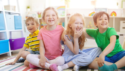 Group of children sitting indoors on the floor and looking in the camera.