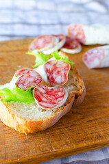 Sandwich with Catalan thin sausage with mold - fuet, on a wooden cutting board. Vertical orientation.