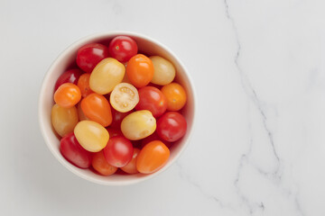 Yellow, orange and red cherry tomatoes in a white bowl
