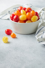 Yellow, orange and red cherry tomatoes in a white bowl