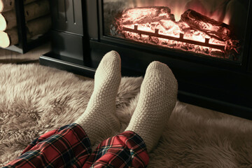 Man in knitted socks resting near fireplace at home, closeup of legs