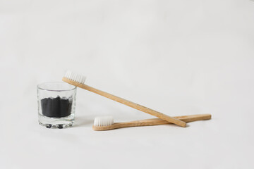 Two eco biodegradable bamboo toothbrushes and activated charcoal in glass on white background