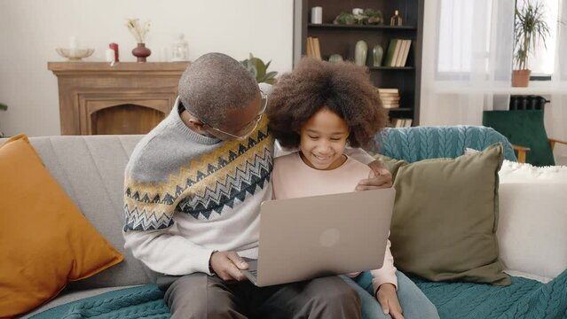 Internet communication. Cheerful african american grandfather and his granddaughter video calling to family via laptop