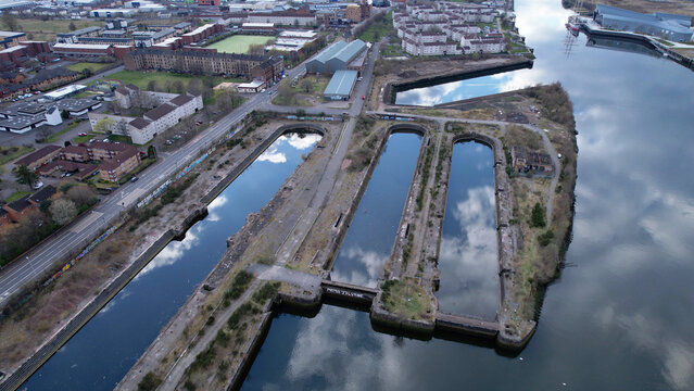 Aerial image over the River Clyde towards Govan in Glasgow, Scotland. A bright sunny day with sky reflections in unused docks giving appearance of huge arched windows like a cathedral.