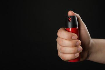 Fototapeta premium Man holding pepper spray on black background, closeup. Space for text