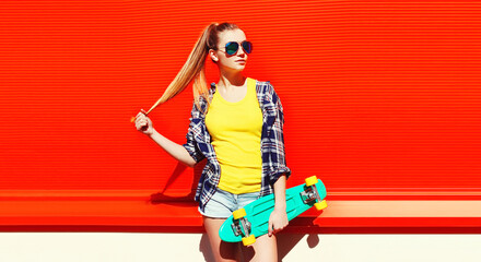 Portrait of stylish young woman with skateboard wearing colorful on vivid background