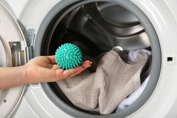 Woman putting green dryer ball into washing machine, closeup