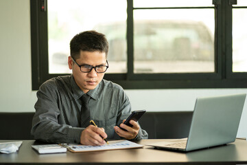 Businessman Holding Pen and Smartphone for Calling Marketing Consulting Analyst with Partner With the calculator, laptop, computer, and graph charts for calls. Marketing Consultant