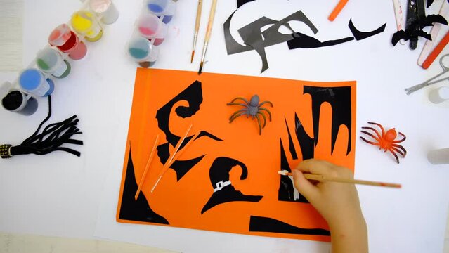 Child making card for the holiday of halloween. Funny crafts from pieces paper. Halloween decor. The concept for Halloween. DIY. Children's art project, a craft for children.