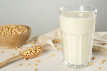 Glass with fresh soy milk and grains on white wooden table, closeup
