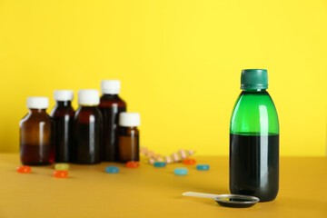 Bottle of cough syrup and dosing spoon on yellow background. Space for text