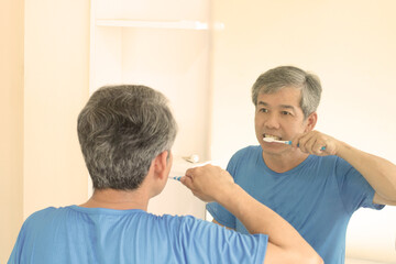 Smiling mature man brushing teeth in bathroom. Happy middle aged looking in mirror while using toothbrush with whitening toothpaste. guy cleaning teeth in the morning time.