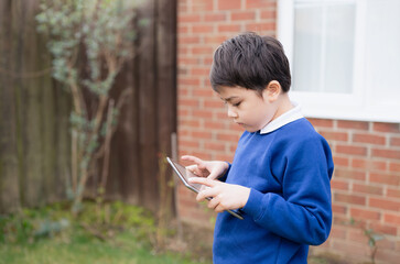Happy Child boy holding tablet pc standing outside waiting for School bus, Portrait Kid playing...
