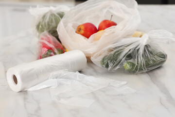 Fototapeta na wymiar Plastic bags with different fresh products on white marble table