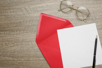 Red envelope with blank letter, pen and glasses on wooden table, flat lay. Space for text