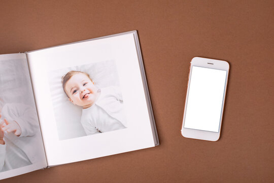 Baby's photo book and mobile phone mock up on brown background . Children's emotional portrait.Cute toddler boy