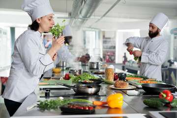Head cook smelling fresh green herbs while sous chef cutting organic vegetables for gourmet cuisine dish. Food industry worker preparing ingredients for dinner service held at restaurant.