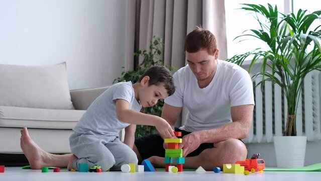 Playtime. kid boy and father play builders in nursery at home. dad playing colorful blocks with his little son, boy building big tower, spending free time together at home interior.