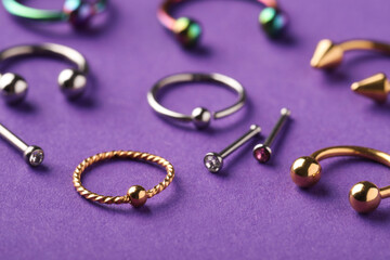 Stylish jewelry for piercing on violet background, closeup