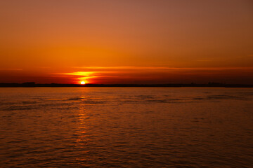 River at sunset. Bright orange sky with the sun touching the horizon