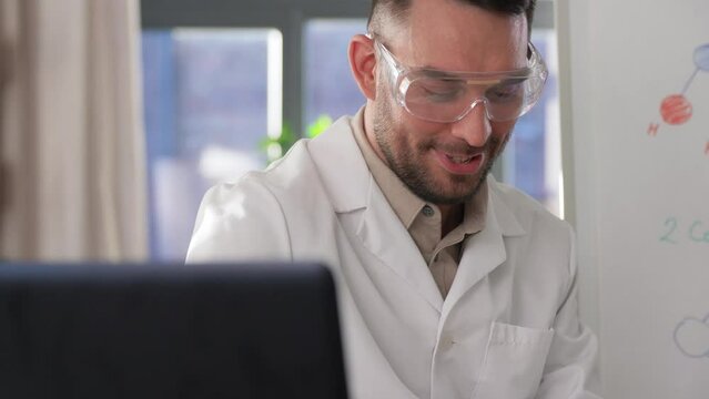 distance education, school and science concept - happy smiling male chemistry teacher in earphones with laptop computer having online class and showing molecular model on flip chart at home office