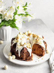 Sliced carrot cake with cream cheese frosting decorated with walnuts and Easter decor with flowers on white background.