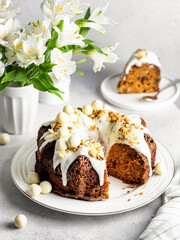 Easter Still life Sliced carrot cake decorated with cream cheese frosting, walnuts and Easter decor with flowers on white background.